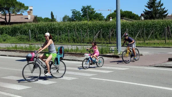 Woman and two children riding bikes across a striped crosswalk.
