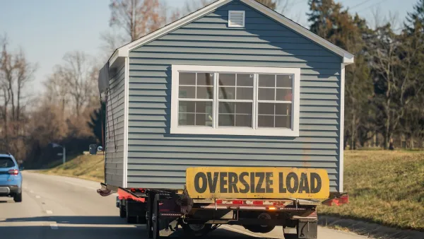 Grey mobile home with yellow "Oversize Load" sign being towed on road.