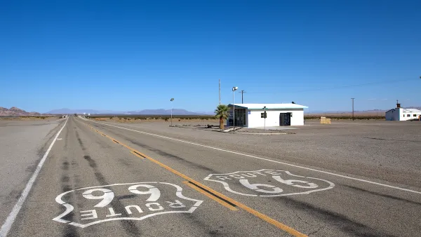 Low shot of Route 66 signs on asphalt with small abandoned building on roadside on old Route 66 near Amboy, California.
