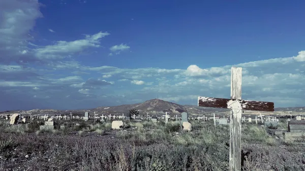 Old cemetery with weathered wooden cross grave markers in Goldfield, Nevada with mountain in background and blue sky.
