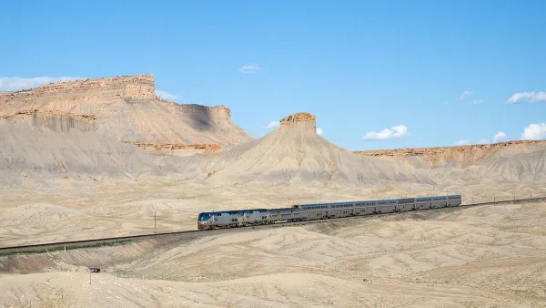 An Amtrak train passing through desert landscape with mesas in Utah.