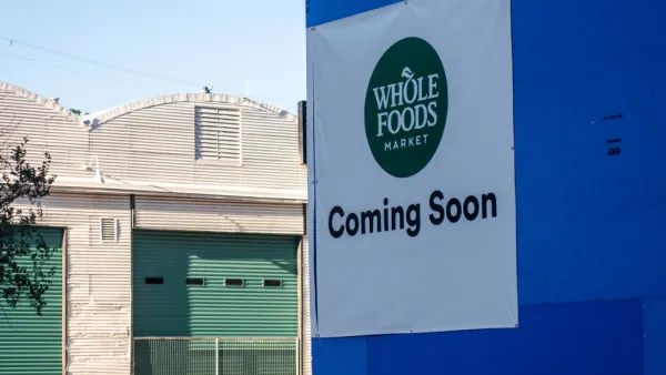 Austin, TA sign reading "Whole Foods Coming Soon" adorns a blue wall across the street from warehouses.