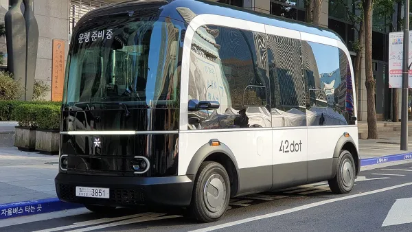 A small boxy driverless shuttle pulled up to a curb.
