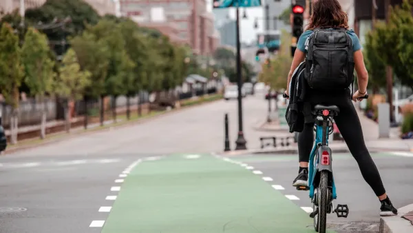 A person on a bike waits at an intersection by leaning against the curb.