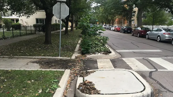Zebra crosswalk with raised curb extensions and bioswale on small street with parked cars and mature trees.