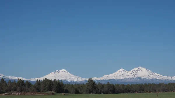 The Three Sisters, snow-covered mountains in Central Oregon, are visible in the distance beyond a farm.