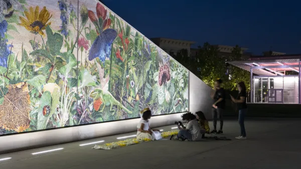 People post for photos in front of a colorful mural in the evening.