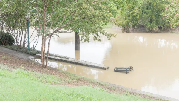 The trees, benches, and other landscape elements of a park are submerged in brown flood waters.