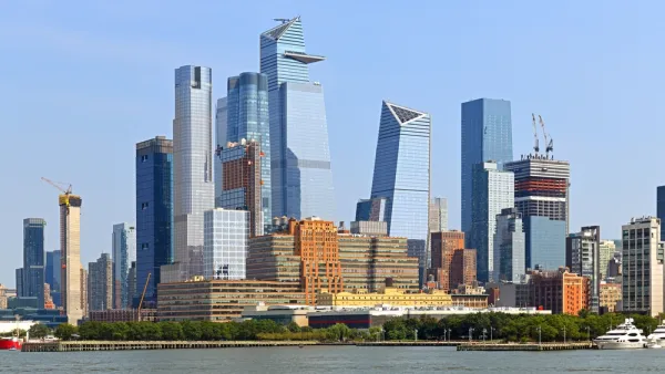 A large group of glass covered skyscrapers rises above the Hudson River in Manhattan, with several new buildings under construction visible too.