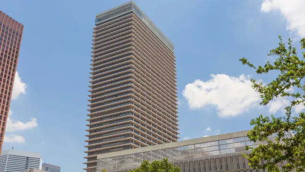 A high-rise building is seen fromt he ground, framed by an assortment of tall and shorter buildings.