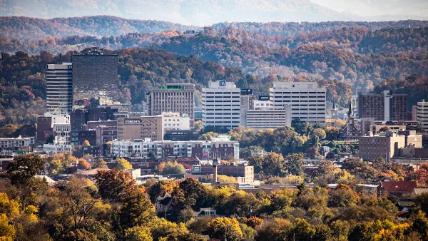 An aerial view of downtown Knoxville, Tennessee, with rolling hills and autumn foliage in the background.