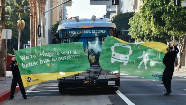 Bus driving through green banner held by two Metro employees at inauguration of new bus lane in downtown Los Angeles.