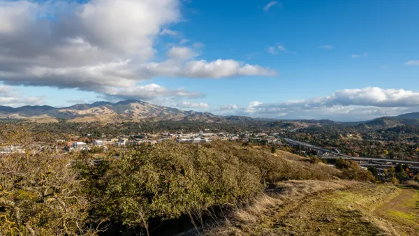 A broad valley with two tall peaks in the background. In the foregound, but far below the view from the hill where the photo was taken, large freeways are visible.