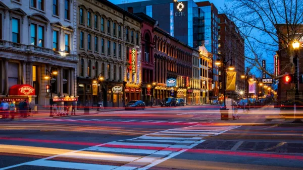 A Downtown Louisville street at night, with the lights of passing shown with a blurred effect.