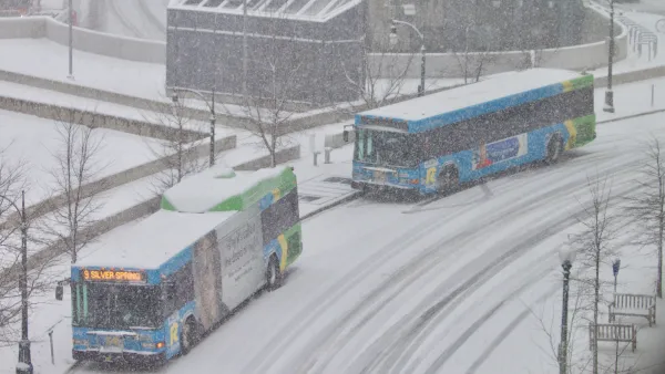 Two buses pull up to a station on a snowy day.