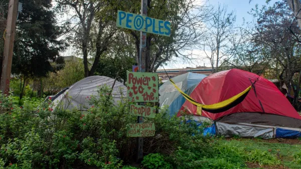 Tents fpor people experiencing homelessness are surrounded by signs that impart messages of resistance to change.