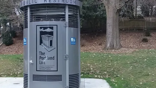 Portland Loo modular gray public bathroom booth sits on concrete slab with green lawn and tree in background in a park in Portland, Oregon