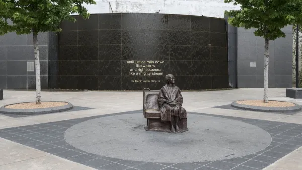 Bronze statue of Rosa Parks sitting on bus bench in center of plaza by Dallas transit station.