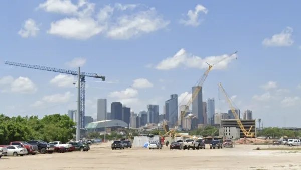 Dirt lot with construction cranes and parked cars with downtown Houston skyline in background