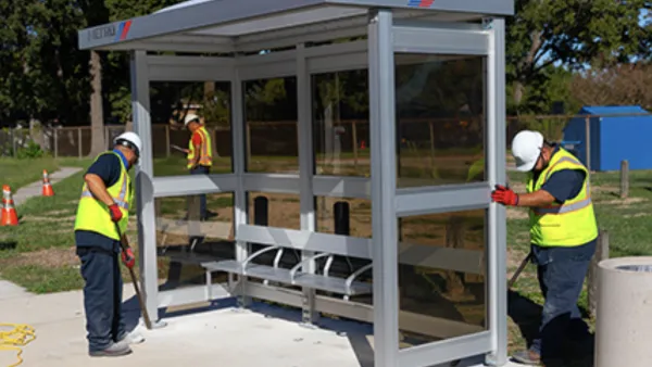 Workers in yellow safety vests installing a bus station shelter in Houston, Texas.