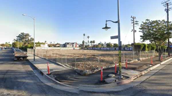 Google street view of vacant fenced-in dirt lot in South Los Angeles with graffiti on wall in background.