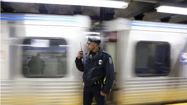 Transit police officer standing on subway platform with blurred train passing behind him.
