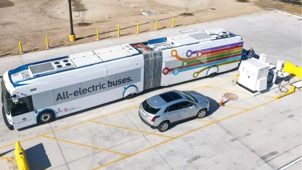 Aerial view of electric bus parked next to silver SUV in parking lot in Austin, Texas. Bus says "All eelctric buses" on side.