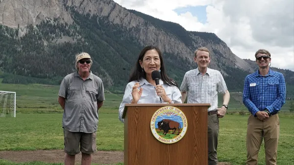 Sec. Deb Haaland speaking at dais outdoors with Colorado mountains in background and three officials standing behind her announcing protection of Thompson Divide.
