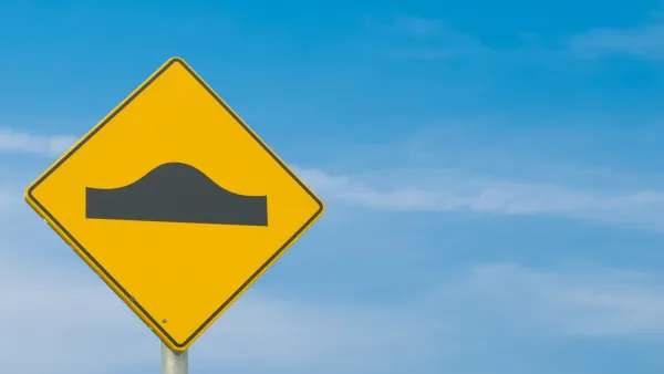 A yellow sign street sign showing the symbol for a speed bump: a simple black bump.