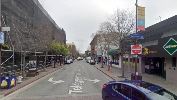A narrow, one-way street is lined with businesses.