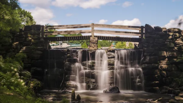 A footbrinde crosses over a small cascade of flowing water on a sunny day in Yonkers, New York.