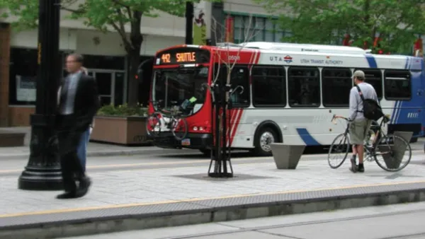 White, red, and blue Utah Transit Authority bus at stop with man standing on sidewalk next to bicycle