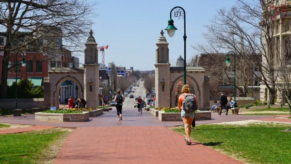 An image of the Sample Gates at the entrance of the college campus of Indiana University Bloomington, with a street and the city in the background.