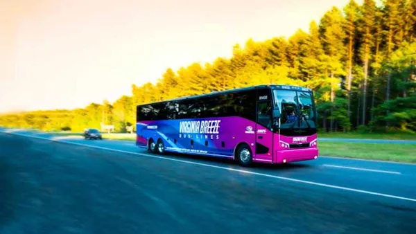 Purple Virginia Breeze intercity bus driving down blurred road with trees on roadside.