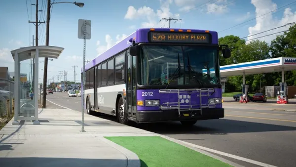 Purple buss pulls up to bus stop in green bus lane.
