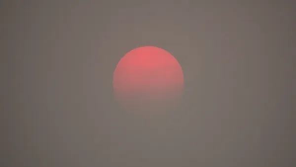 A red sun appears on the horizon, as obscured by haze from wildfire smoke.