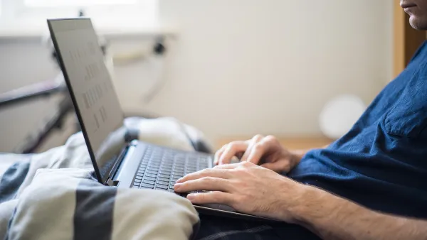 A man working from home works on his laptop from bed.