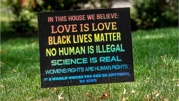 A rainbow colored sign planted in the front yard of a typical suburban home reads, "In this house we believe love is love, black lives matter, no human is illegal, science is real, women's rights are human rights. In a world where you can be anything, be kind."