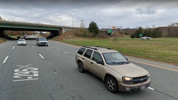 A two-lane highway cuts through a small canyon. The photo is taken from the perspective of a vehicle on the road.