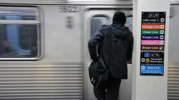 View from back of person in black clothes and hat waiting to board train at Chicago train station with blurry train in front of them.