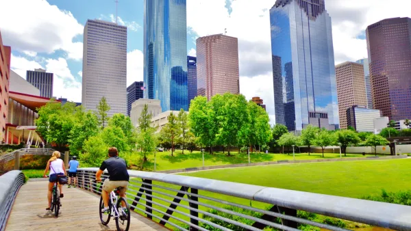 Two cyclists on a wooden bike bridge across a bayou with downtown Houston skyline in background