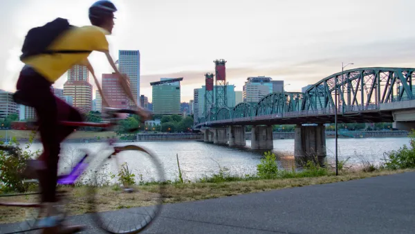 Cyclist on bike path in Portland, Oregon with bridge over river and city skyline in background.