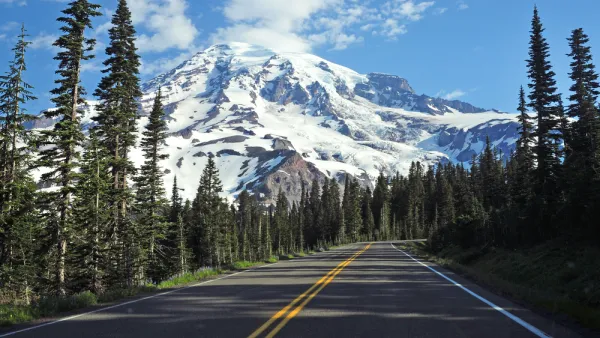 Two-lane asphalt road in Washington state with pine trees along sides and Mt. Rainier in background