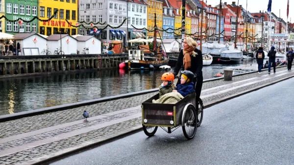 Woman riding cargo bike with two small children on Copenhagen street next to a canal