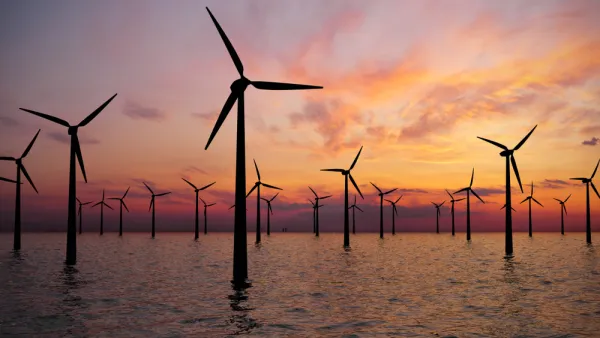 Offshore wind turbines in water against a sunset sky