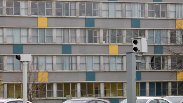 Two white traffic enforcement cameras above a road in Ottawa, Canada with a colorful multistory building in background