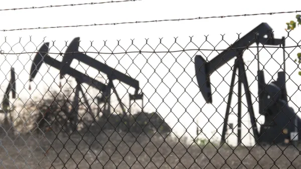 View of black oil wells behind chain link fence with barbed wire top
