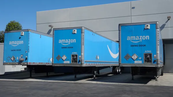 Three blue Amazon delivery trucks at bays at a distribution center