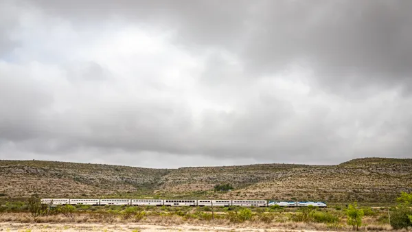 Amtrak Sunset Limited train viewed from the side passing low desert hills in West Texas