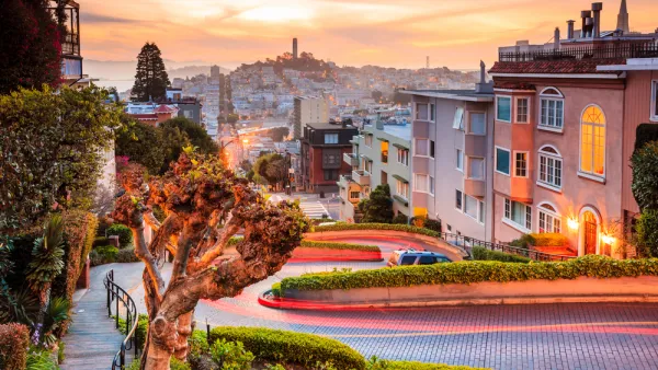 View of downtown San Francisco from top of windy street at sunset with Coit Tower in distance